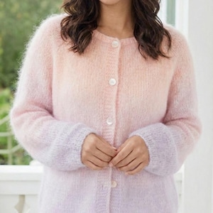 May include: A button-down cardigan in a soft, fluffy knit. The sweater features a gradient color scheme, transitioning from a light peach at the top to a lavender hue at the cuffs. The long sleeves and round neckline add to its cozy appeal.