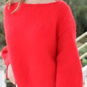 May include: A vibrant red long-sleeved sweater with a fuzzy, textured knit finish. The garment features a wide boat neckline and a relaxed fit, with ribbed cuffs at the wrists and a straight hemline that sits at the waist, providing a soft appearance.