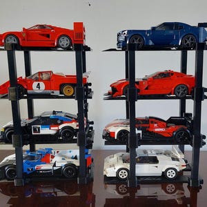 Può includere: Una collezione di modellini di auto in vari colori, tra cui rosso, blu, bianco e nero, esposti su scaffali neri a più livelli. Le auto sono disposte in un ambiente simile a un garage.