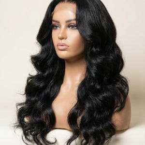 May include: A black, wavy wig displayed on a mannequin head. The wig has long, flowing curls and a realistic hairline. The mannequin has a fair complexion and is set against a neutral background, emphasising the wig's texture and colour.