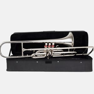 Puede incluir: Un tromb&oacute;n plateado con detalles rojos, dentro de un estuche negro abierto. El instrumento es brillante y refleja la luz. El estuche rectangular est&aacute; forrado con tela negra, proporcionando protecci&oacute;n para el instrumento musical.