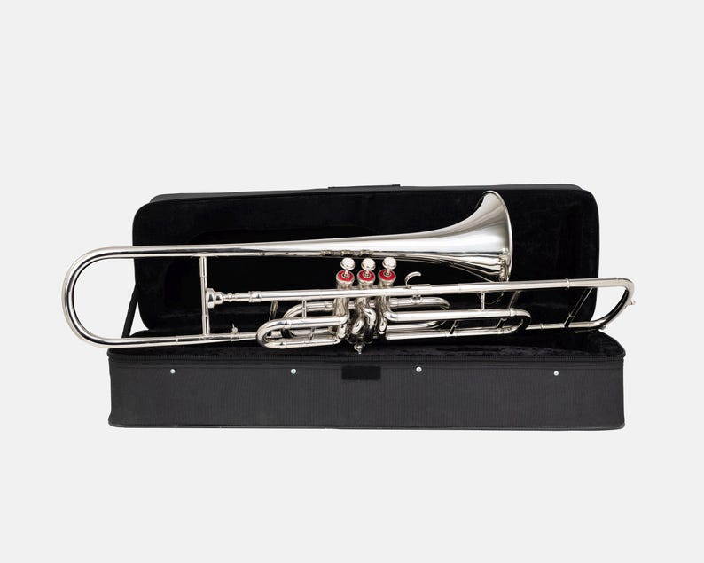 Puede incluir: Un tromb&oacute;n plateado con detalles rojos, dentro de un estuche negro abierto. El instrumento es brillante y refleja la luz. El estuche rectangular est&aacute; forrado con tela negra, proporcionando protecci&oacute;n para el instrumento musical.
