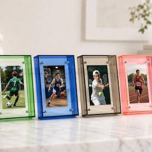May include: Four rectangular acrylic photo frames in green, blue, grey, and pink. Each frame features a clear centre panel held by four silver-toned metal corner bolts, displaying photographs of athletes playing football, basketball, tennis, and track.