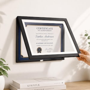 May include: A black document frame with a hinged front opening, displaying a Certificate of Achievement for Sophia Anderson for Academic Excellence, dated May 25th, 2024, featuring a navy blue mat and a gold-toned border around the certificate.