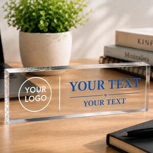 Peut inclure: Un présentoir de bureau rectangulaire en acrylique transparent avec un graphique circulaire blanc portant le texte YOUR LOGO à gauche, séparé par une ligne verticale d'un texte bleu indiquant YOUR TEXT avec un losange et YOUR TEXT en dessous.