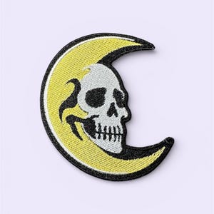 May include: Embroidered patch featuring a white skull on a yellow crescent moon with a black border. The patch has a detailed design, suitable for jackets, bags, or other fabric items. The patch is a gothic or Halloween-themed accessory.