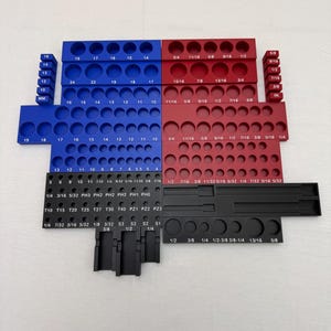 May include: A multi-piece tool organizer set featuring blue, red, and black modular trays with circular cutouts for bits and sockets. Each section is clearly labeled with printed size markings in inches and millimeters for organized storage.