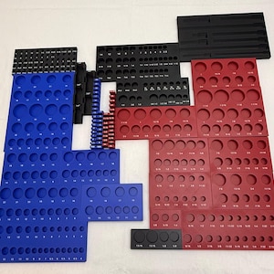 May include: A collection of modular tool organisers in black, blue, and red, featuring various circular cutouts for sockets and rectangular slots for wrenches. Each organiser is labelled with printed numerical size markings for identification.