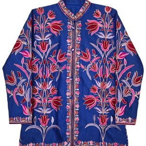 May include: A long-sleeved blue jacket featuring a mandarin collar and a front button closure. The garment is decorated with intricate floral embroidery in shades of pink, red, and light purple, covering the front panels and sleeves.