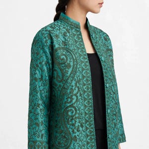 May include: A teal jacket featuring dark green intricate floral and paisley embroidery throughout. The jacket has a mandarin collar, three-quarter length sleeves, and a front button closure with matching fabric-covered buttons.