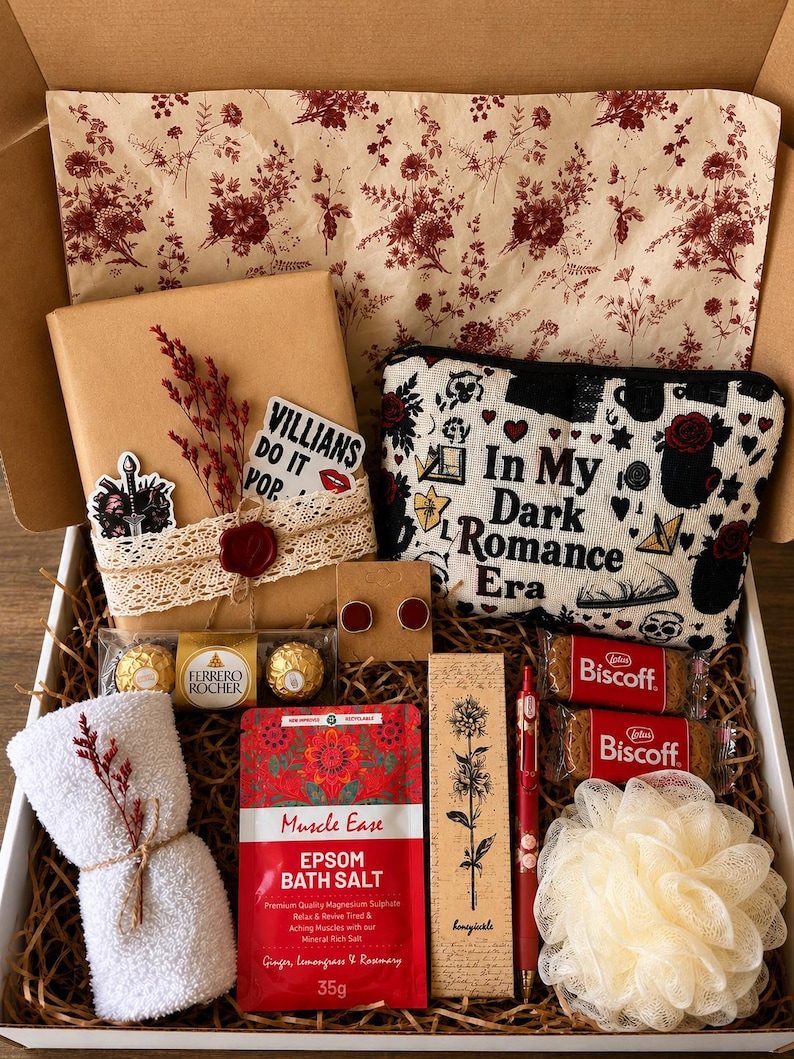 Op de afbeelding: Een geschenkdoos gevuld met diverse items. Inclusief een verpakt pakket met een sticker met de tekst "Villains Do It Pop", een cosmetische tas met de tekst "In My Dark Romance Era", een handdoek, badzout, oorbellen, chocolaatjes, koekjes, een pen en een loofah.
