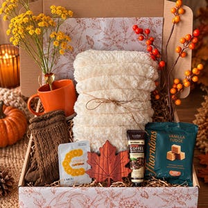 Peut inclure: Un coffret cadeau contenant une écharpe duveteuse crème, une tasse orange, des chaussettes en tricot marron, un masque à l'argile à la vitamine C, un ornement en bois en forme de feuille d'érable, une crème pour les mains au café et du fudge.