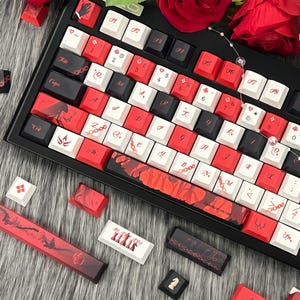 May include: A black mechanical keyboard with red and white keycaps. The keycaps feature various symbols and letters, with some keys displaying decorative patterns. Additional keycaps are scattered around the keyboard, and the overall aesthetic is a blend of functionality and design.