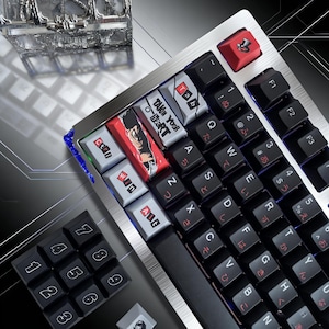 May include: A silver and black mechanical keyboard with custom keycaps. The keycaps feature Japanese characters and graphic designs, including a character portrait and the text "TAKE YOUR HEART". A separate number pad is also visible.