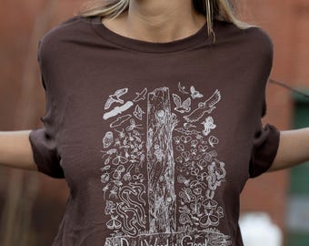 May include: A dark brown short-sleeve t-shirt featuring a white line-art graphic of a tree trunk surrounded by various insects, birds, and small animals. The text "Dead Wood is Good" is printed in white at the bottom of the graphic design.