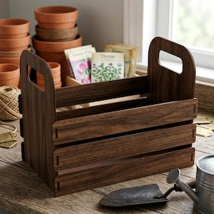May include: A dark brown wooden crate with a handle, designed for gardening supplies. The crate has a slatted design and holds seed packets labeled "Sweet Pea" and "Thyme". Other gardening tools and terracotta pots are visible.