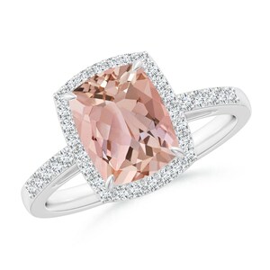 May include: A ring featuring a large, rectangular, peach-colored gemstone surrounded by a halo of smaller, clear gemstones. The band is silver-colored and also set with small, clear gemstones. The ring is set against a white background.