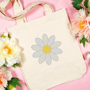 May include: A white canvas tote bag with a light blue and yellow embroidered daisy.