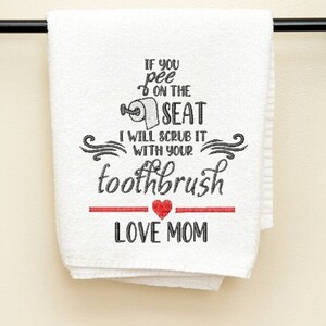 May include: White bathroom towel with black text that reads "IF YOU pee ON THE SEAT I WILL SCRUB IT WITH YOUR toothbrush LOVE MOM." The text is embroidered in a playful font, with a red heart and line.