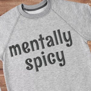May include: A grey sweatshirt with the text "mentally spicy" embroidered in black.