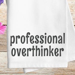 Może przedstawiać: Biały ręcznik kuchenny z czarnym haftem z tekstem "profesjonalny rozmyślaniec".