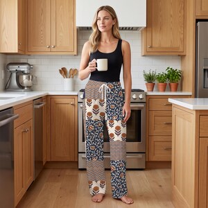 May include: A black sleeveless top paired with loose-fitting lounge pants featuring a multi-panel patchwork design. The pants display alternating sections of floral motifs in orange and white, dark blue vine patterns, and brown and white chevron stripes.