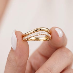 May include: A gold ring featuring a double-band design with a wavy silhouette. The bottom band is embedded with a row of small, clear, round-cut stones. The interior of the band is engraved with the text FIOR in a clear, sans-serif font.