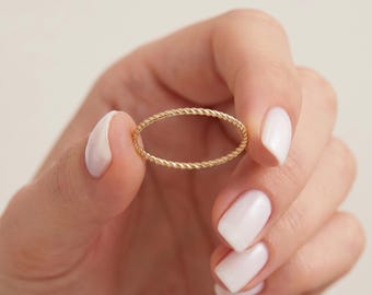 May include: A thin, gold-colored ring featuring a delicate, twisted rope-like texture. The band is circular and maintains a consistent, slender width throughout its entire circumference, showcasing a polished, metallic finish with a subtle sheen.