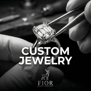 Peut inclure: Une bague argentée avec une grande pierre centrale taille émeraude maintenue par quatre griffes. Le texte CUSTOM JEWELRY est affiché, accompagné d'un logo de cerf et du texte FIOR LUMIN JEWELLERY dans un style monochrome noir et blanc.