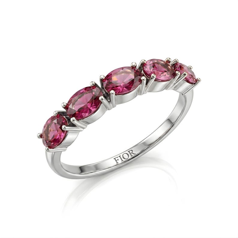 Op de afbeelding: Zilveren ring met vijf ovale, helder roze edelstenen. De edelstenen zijn gezet in individuele prong-instellingen. Het woord "FIOR" is gegraveerd aan de binnenkant van de ringband. De ring wordt op een witte achtergrond getoond.