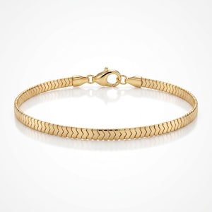 Op de afbeelding: Een goudkleurige visgraatkettingarmband met een plat, flexibel schakelontwerp en een gepolijste afwerking. De armband wordt vastgezet met een karabijnsluiting, wat zorgt voor een consistente en gladde uitstraling over de gehele lengte van de ketting.