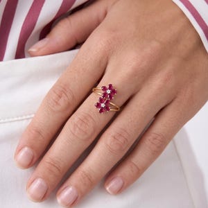 Puede incluir: Un anillo de oro con dos motivos en forma de flor, cada uno compuesto por cinco rub&iacute;es de color rosa intenso en talla marquesa que rodean un peque&ntilde;o diamante blanco central en talla redonda. El aro es fino y pulido, con dise&ntilde;o abierto.