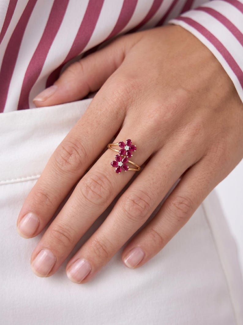 Puede incluir: Un anillo de oro con dos motivos en forma de flor, cada uno compuesto por cinco rub&iacute;es de color rosa intenso en talla marquesa que rodean un peque&ntilde;o diamante blanco central en talla redonda. El aro es fino y pulido, con dise&ntilde;o abierto.