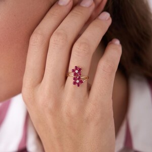 Puede incluir: Un anillo de oro con dos motivos en forma de flor, cada uno compuesto por cinco rub&iacute;es rojos de talla pera que rodean un peque&ntilde;o diamante blanco central. La banda es fina y dividida, conect&aacute;ndose a la base de cada dise&ntilde;o floral.