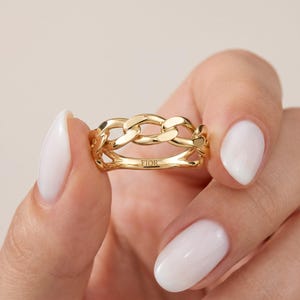 May include: A polished gold ring featuring a continuous chain link design. The band has a smooth, reflective surface and the word FIOR is clearly engraved on the inner side of the metal band, showcasing a refined and metallic yellow gold finish.