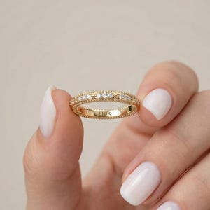 Könnte beinhalten: Ein goldener Ring mit kleinen Diamanten in einem Band. Der Ring hat einen Perlenrand und das Wort "FIOR" ist innen eingraviert. Der Ring wird von einer Person gehalten.