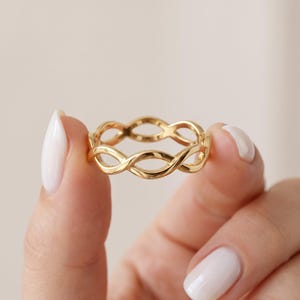 Peut inclure: Une bague en or poli présentant un motif métallique torsadé continu et répétitif de style infini. L'anneau est composé de boucles arrondies, lisses et interconnectées qui créent un design ajouré, avec une finition métallique brillante.