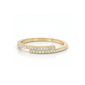 May include: A gold ring with a distinctive, wraparound design. The ring is embellished with small, sparkling stones set along the band. The word "FIOR" is engraved on the inside of the ring. The ring is set against a white background.