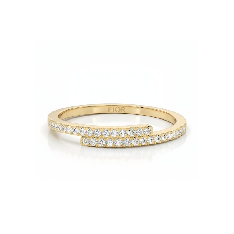 May include: A gold ring with a distinctive, wraparound design. The ring is embellished with small, sparkling stones set along the band. The word "FIOR" is engraved on the inside of the ring. The ring is set against a white background.
