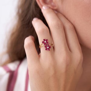 Puede incluir: Un anillo de oro con dos motivos en forma de flor, cada uno compuesto por cinco rub&iacute;es de color rosa intenso en talla pera que rodean un peque&ntilde;o diamante blanco de talla redonda en el centro. El aro es fino y pulido, uniendo los elementos.