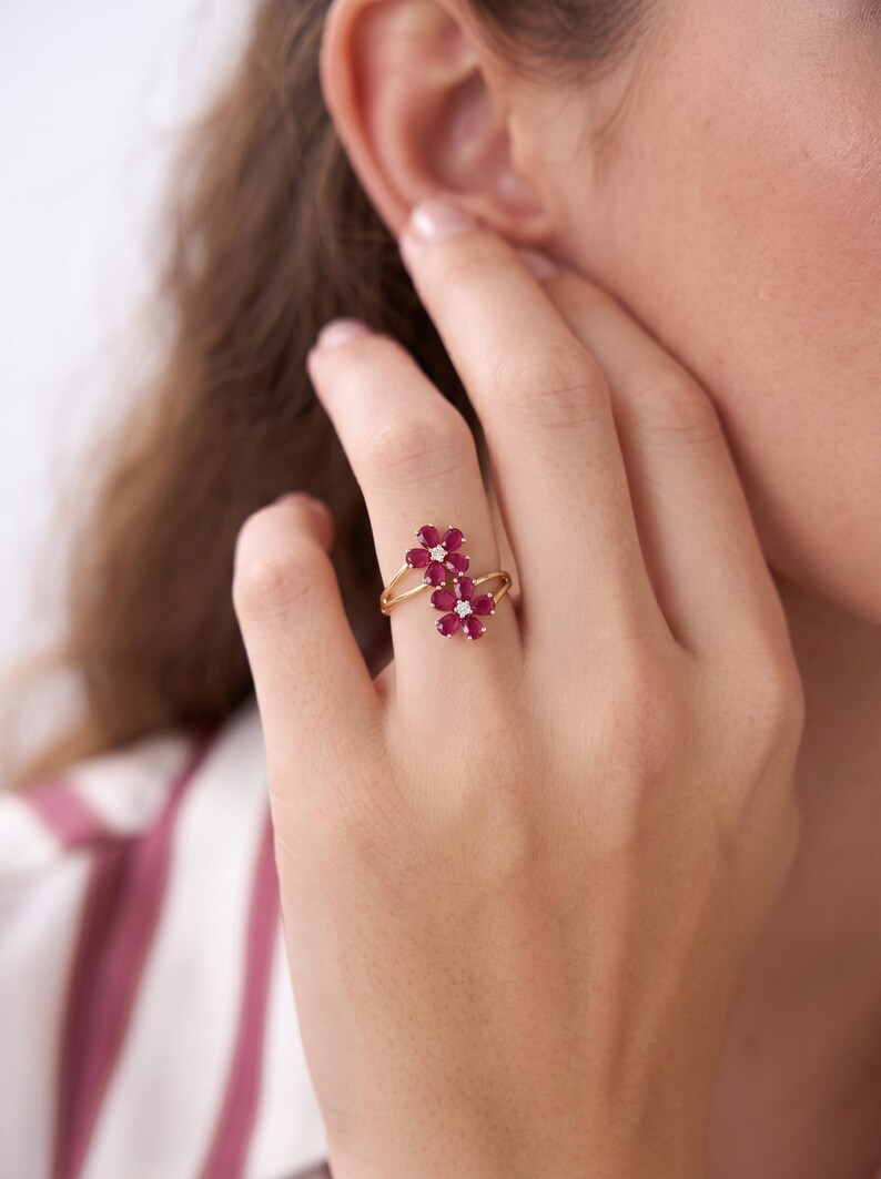Puede incluir: Un anillo de oro con dos motivos en forma de flor, cada uno compuesto por cinco rub&iacute;es de color rosa intenso en talla pera que rodean un peque&ntilde;o diamante blanco de talla redonda en el centro. El aro es fino y pulido, uniendo los elementos.