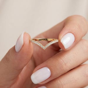 Peut inclure: Une bague en forme de V en or avec une rangée de petites pierres claires serties pavé le long du bord extérieur. L'anneau présente une finition polie et le mot FIOR est gravé en petites lettres capitales sur la surface intérieure de la bague.