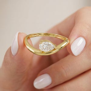 Könnte beinhalten: Ein Goldring mit einem birnenförmigen Diamanten, der in eine geschwungene, offene Ringschiene gefasst ist. Das Metallband hat eine polierte Oberfläche und das Wort FIOR ist auf der Innenseite eingraviert. Das Design zeigt einen facettierten Stein.