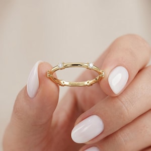 Puede incluir: Un anillo de banda dorada con cuatro piedras pequeñas, transparentes y de corte redondo, espaciadas uniformemente y engastadas en garras. El interior de la banda tiene grabado el texto FIOR. El anillo tiene un acabado pulido y perfil fino.