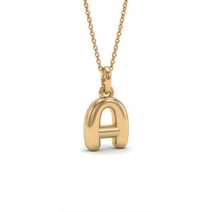 以下が含まれることがあります： 金色のペンダントネックレスで、文字「A」が特徴です。ペンダントは丸みを帯びたバブルスタイルのデザインで、繊細なチェーンから吊り下げられています。ネックレスはおそらく金または金色の金属で作られています。