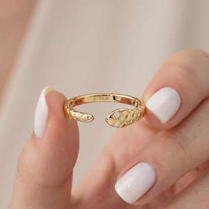 Puede incluir: Un anillo dorado con forma de serpiente, con un diseño texturizado y dos pequeños diamantes. El anillo abierto tiene la inscripción "FIOR".