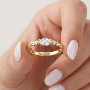 Peut inclure: Une bague en or jaune avec une pierre précieuse centrale transparente taille marquise, encadrée par deux pierres plus petites taille ronde sur un anneau torsadé. L'intérieur de l'anneau porte l'inscription FIOR en lettres capitales.
