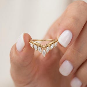 May include: A gold V-shaped ring featuring a series of marquise-cut white stones set along the band. The metal band is engraved with the text FIOR on the inner surface. The design follows a chevron silhouette with stones arranged symmetrically.