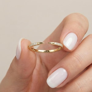 Puede incluir: Un anillo de oro con un diseño dividido, sostenido entre los dedos. El anillo presenta una banda incrustada con pequeñas piedras preciosas transparentes y extremos puntiagudos. La palabra "FIOR" está grabada en el anillo. El anillo es una joya.