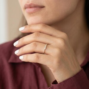May include: A gold ring featuring a linear arrangement of small, glittering stones. The ring is displayed on a finger, with the hand positioned near the face. The ring's design is contemporary and minimalist, suitable for daily wear or special events.